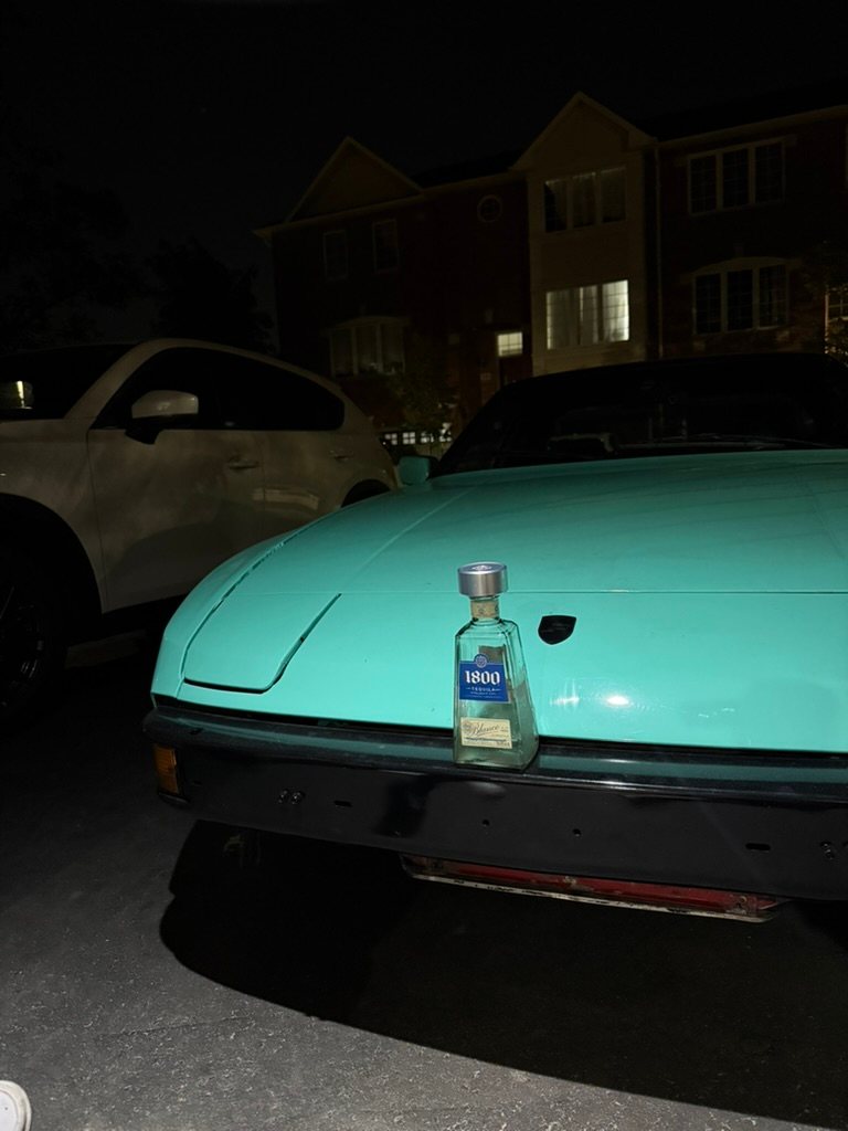The mint Porsche 944 at night with a bottle of 1800 Tequila on the hood